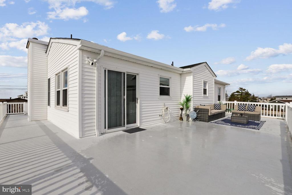 Rooftop deck with white siding, a sliding glass door, and a small outdoor seating area.