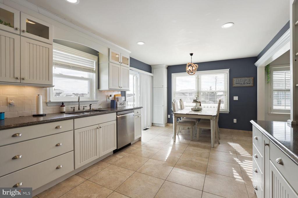 Bright kitchen with white cabinets and dark counters opening to a dining area with a blue accent wall.