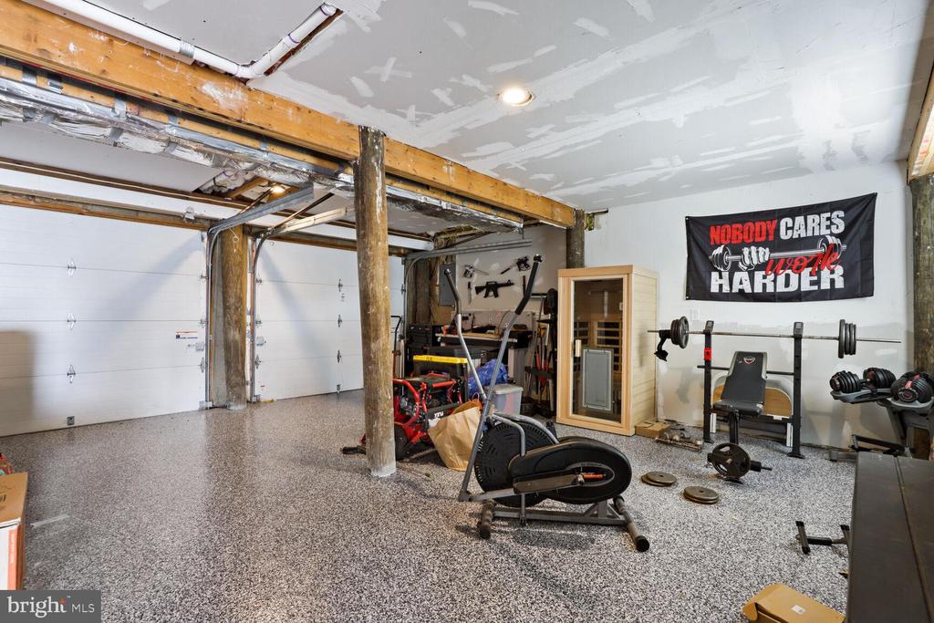 Garage home gym with a sauna, exercise equipment, speckled flooring, and exposed ceiling beams.
