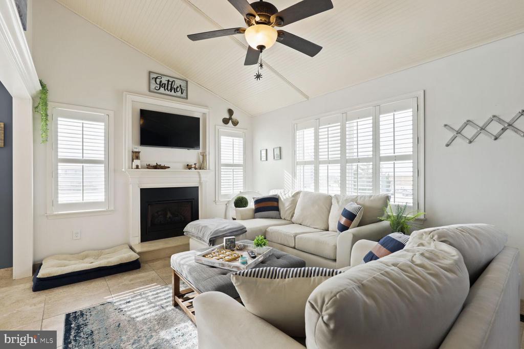 Living room with white sectional sofas, a fireplace, shuttered windows, and a vaulted ceiling.