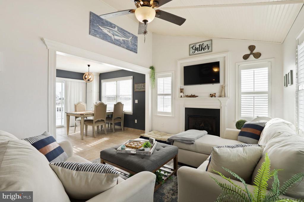 Living room with white sofas and fireplace, opening to a dining area.