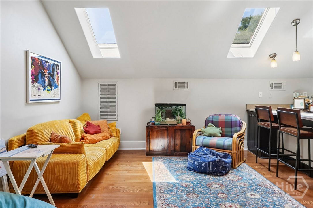 Living room with a mustard-yellow sofa, plaid armchair, blue rug, and two skylights.