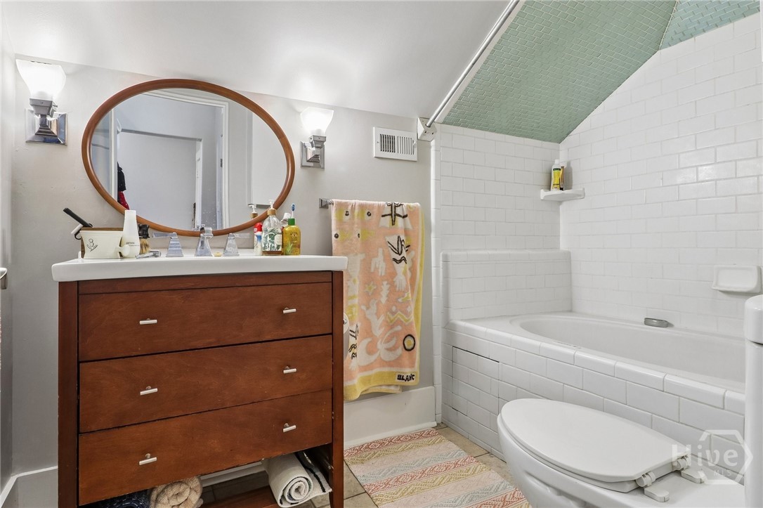 Bathroom with a tiled bathtub, dark wood vanity, oval mirror, and pale green tiled ceiling.
