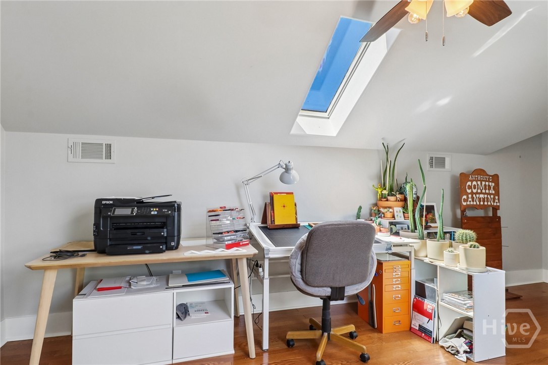 Home office with a skylight, long desk, orange filing cabinet, and potted plants.