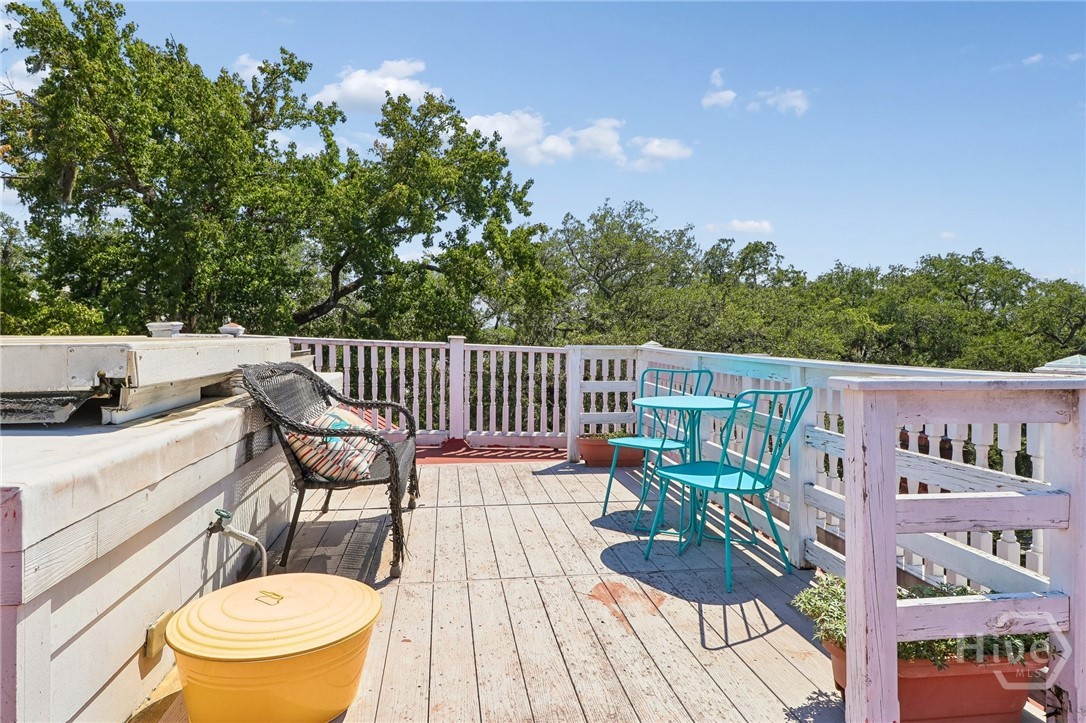 Rooftop deck with turquoise patio furniture, white railings, and leafy trees beyond.