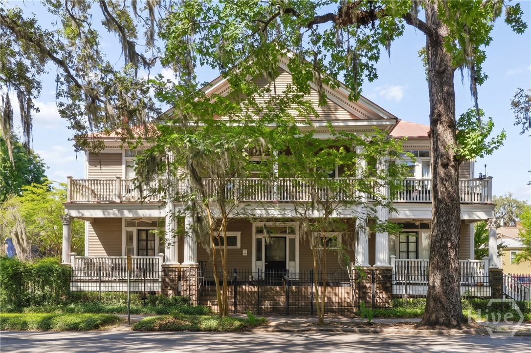 Two-story tan house with white wraparound porches, framed by large trees draped in Spanish moss.