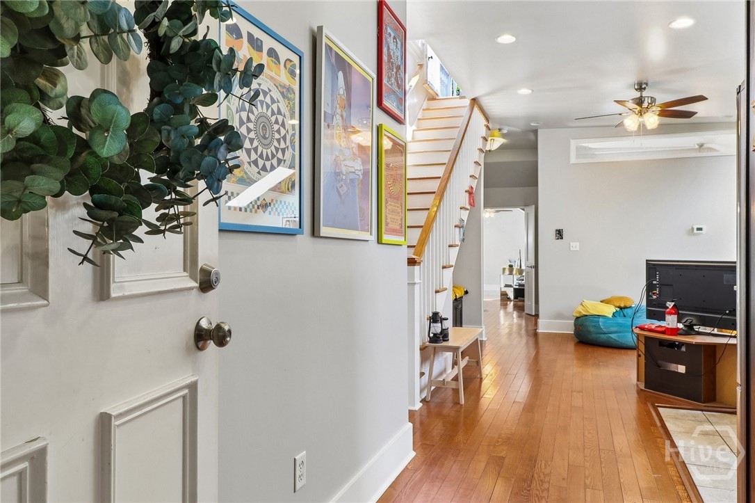 Entry hall with hardwood floors, a staircase, framed artwork, and a leafy plant beside the door.
