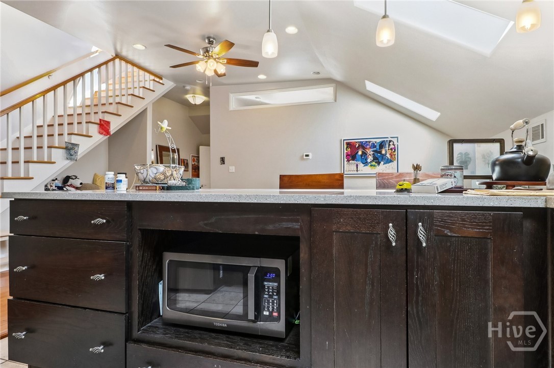 Kitchen island with dark wood cabinets and a built-in microwave, beneath a vaulted ceiling beside a staircase.