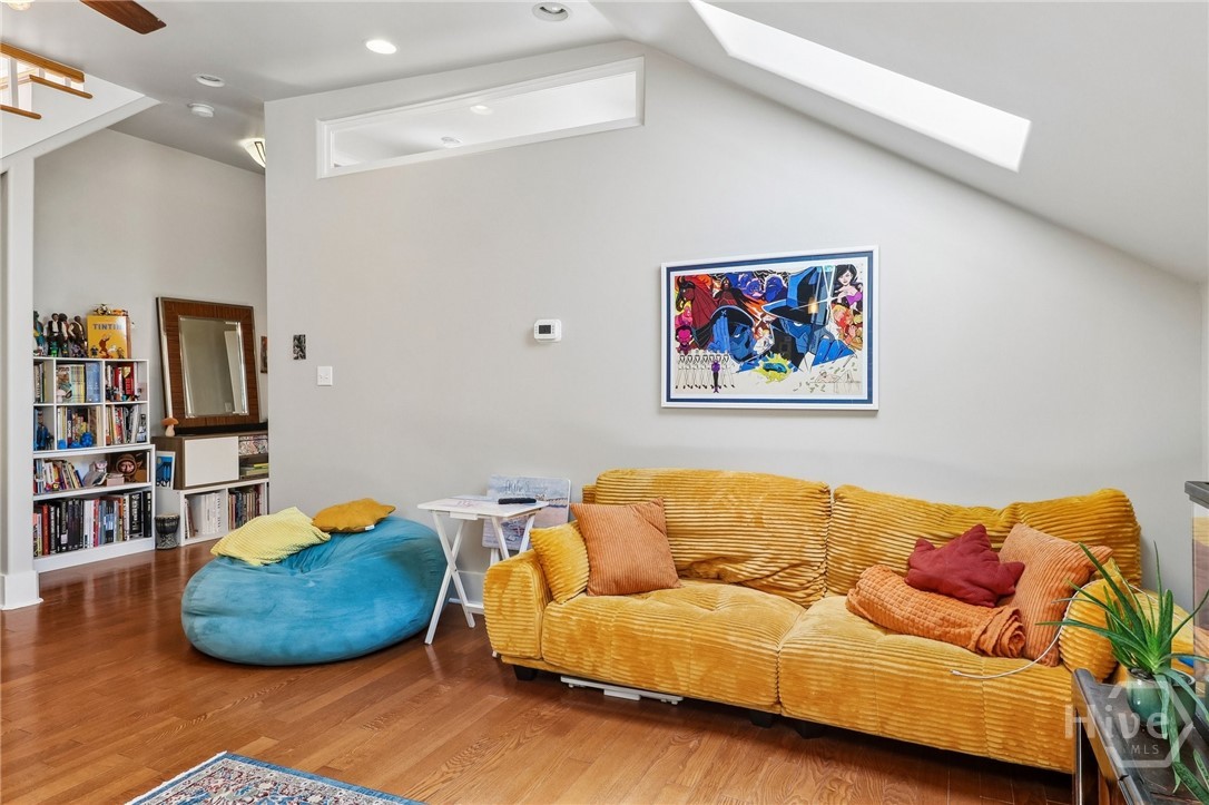 Living room with a mustard-yellow sofa, blue beanbag, hardwood floors, and a skylight.