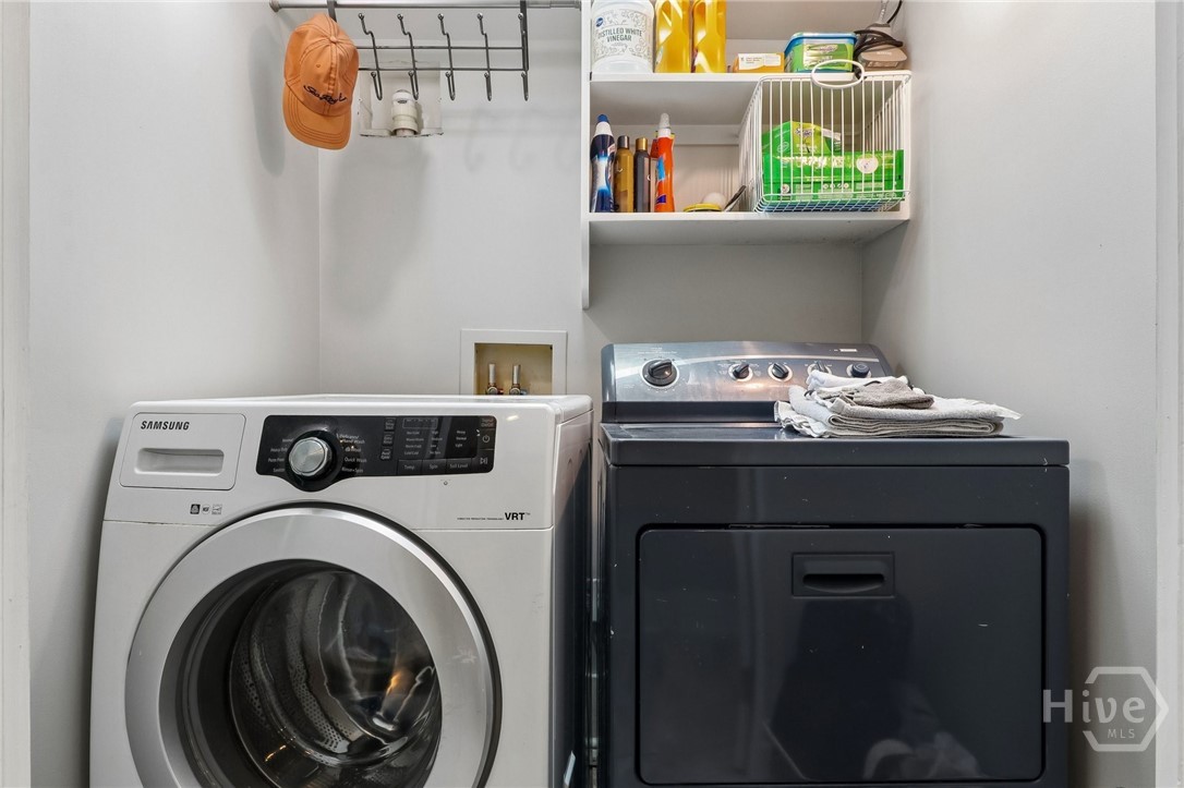 Laundry room with a white front-loading washer, dark dryer, and open storage shelves.