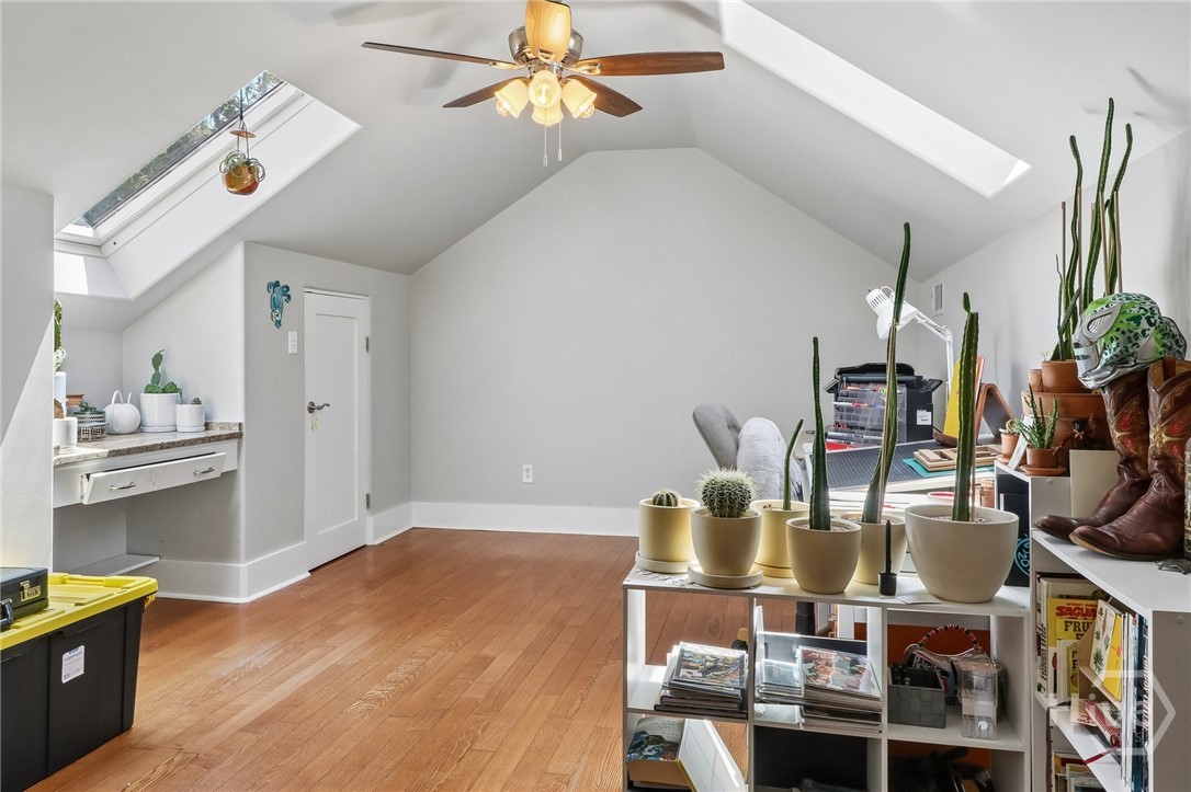 Finished attic room with skylights, hardwood floors, a desk, and potted plants.