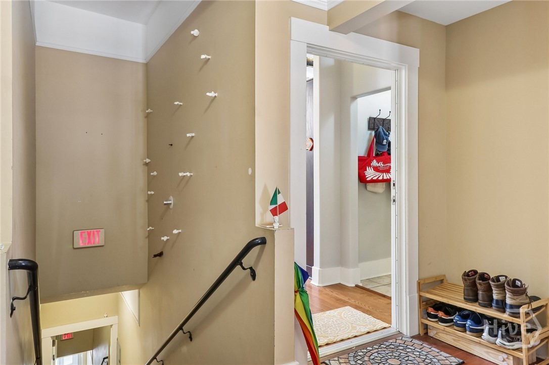 Entry stairwell with black handrails, a doorway to a wood-floored room, and shoes on a rack.