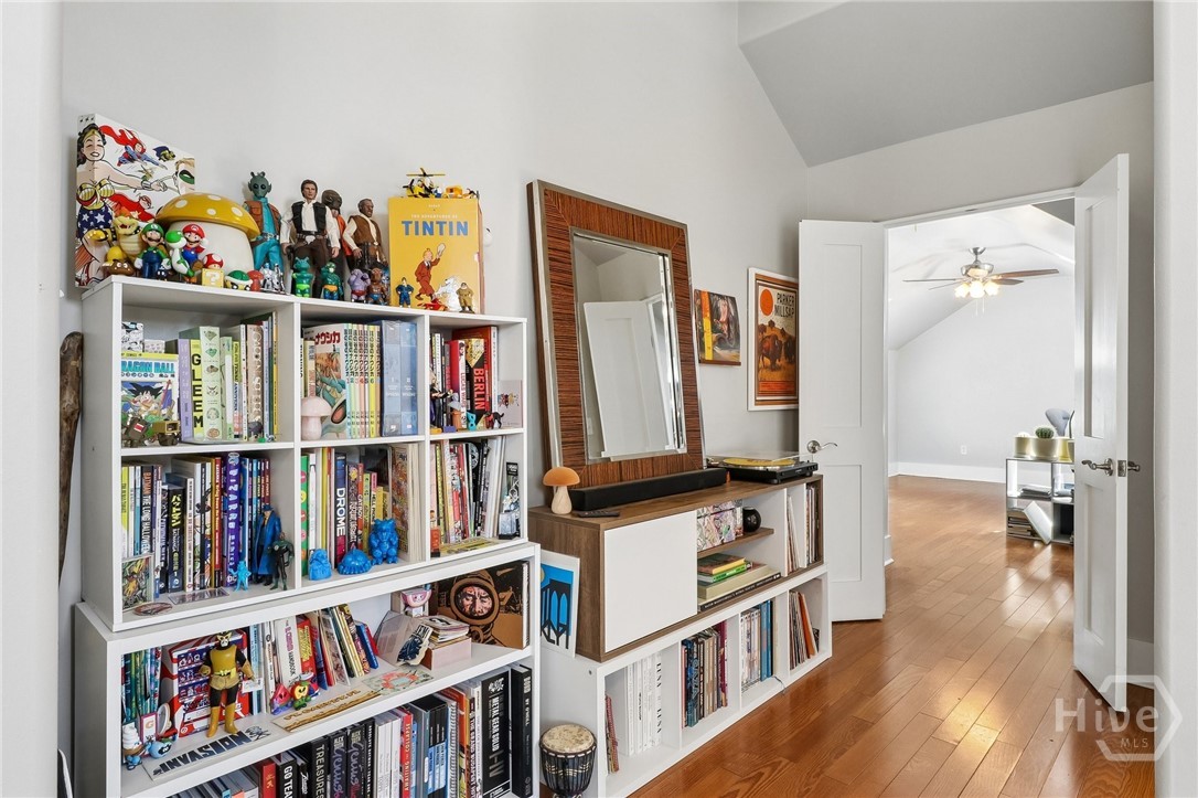 Book-lined room with collectible figures and hardwood flooring leading through an open doorway.
