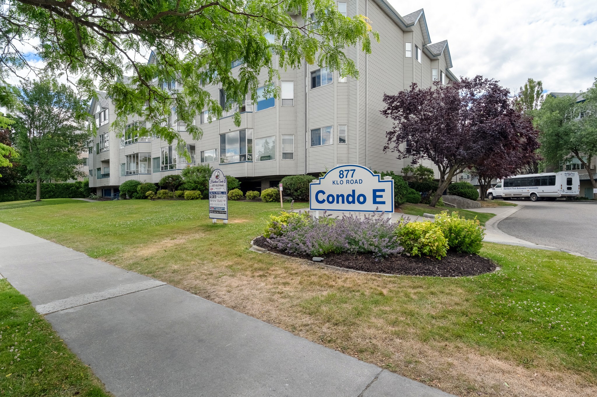 Condo E at 877 Klo Road, a multi-story building framed by mature trees and landscaped grounds.