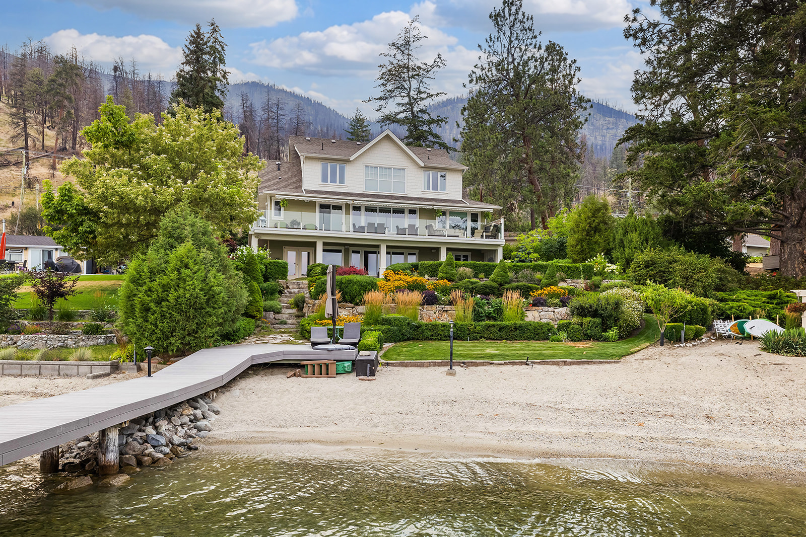 Two-story lakeside house with a broad balcony, landscaped terraces, and a dock over the water.