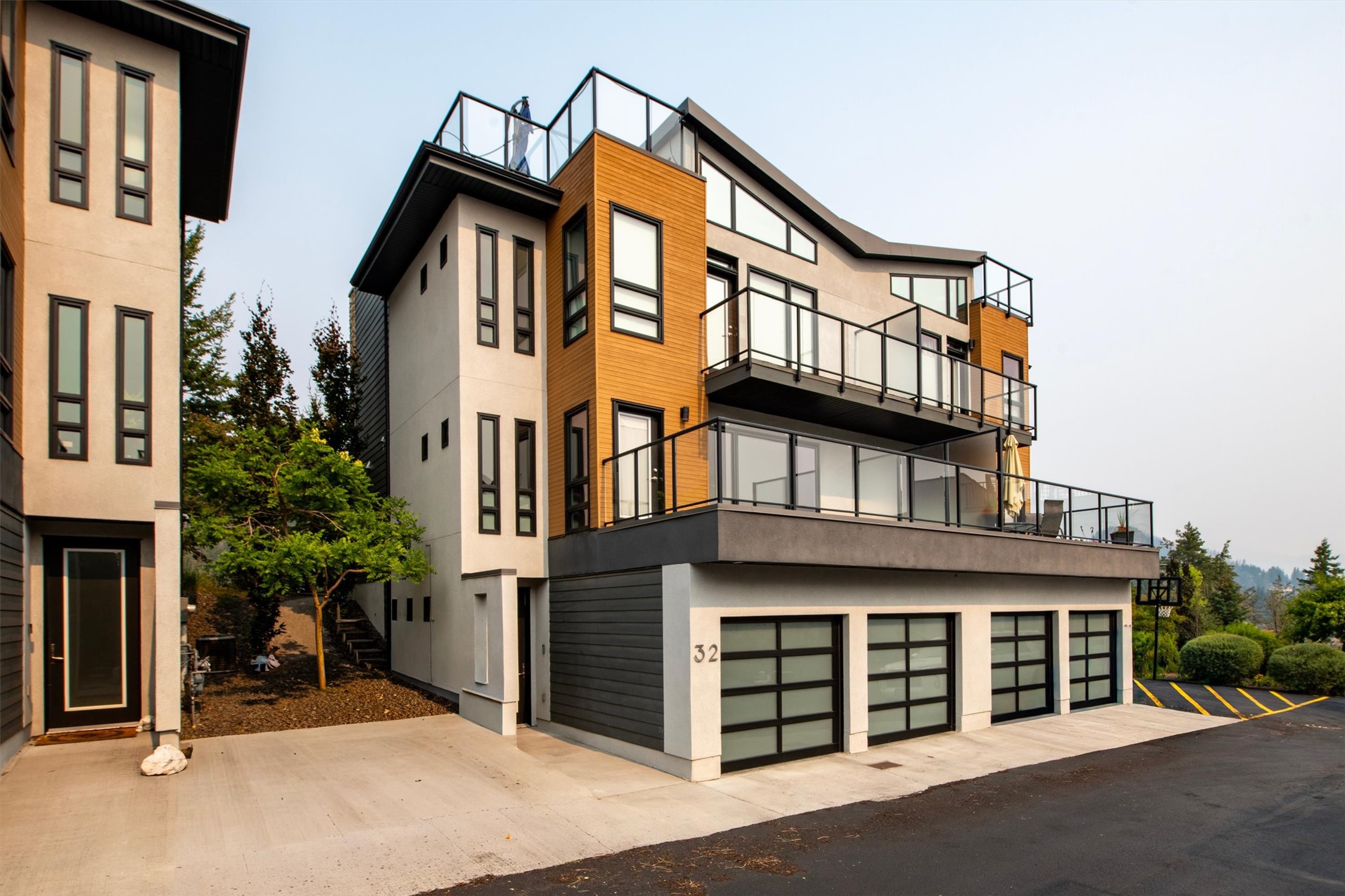 Modern multi-story home with wood siding, glass balconies, rooftop deck, and multiple garage doors.