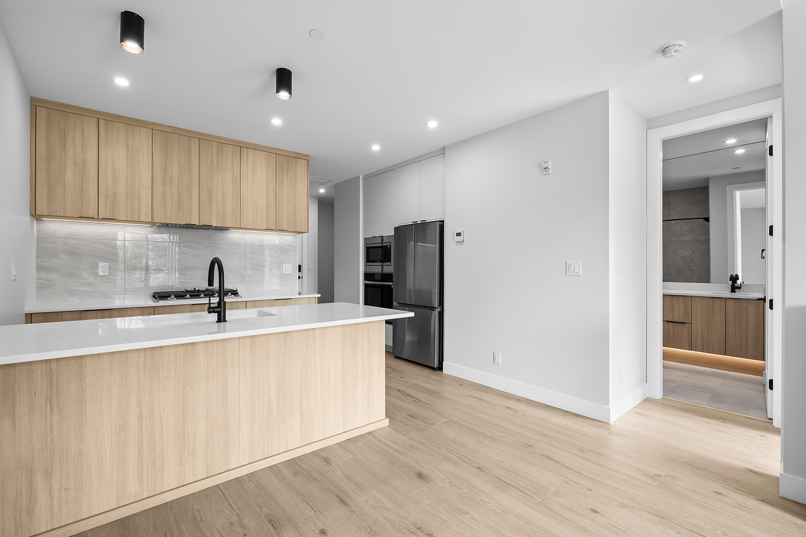 Modern kitchen with pale wood cabinetry, a large island, and stainless steel appliances.