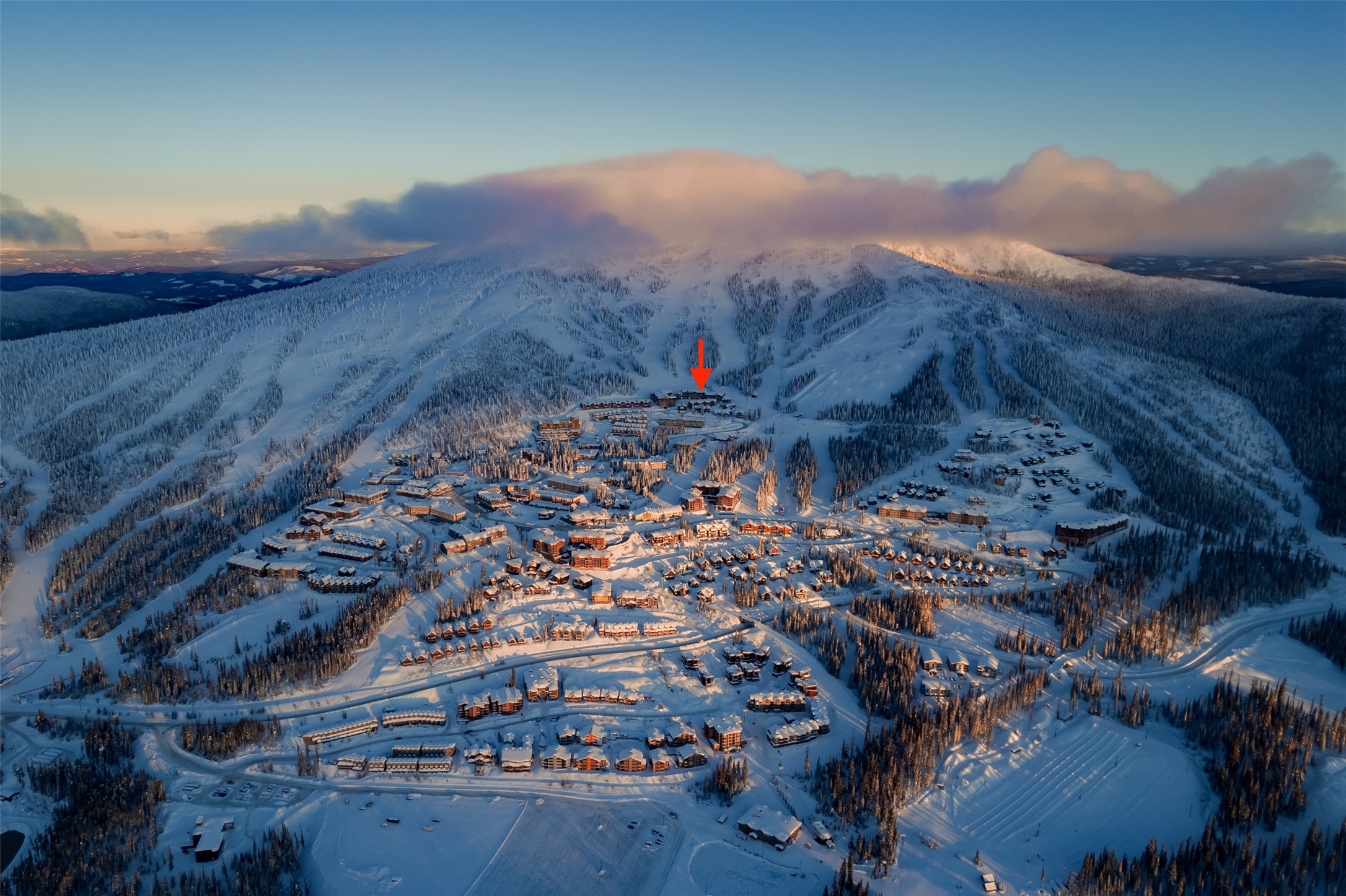 Snow-covered mountain resort with ski runs and buildings; a red arrow marks one near the mountain.