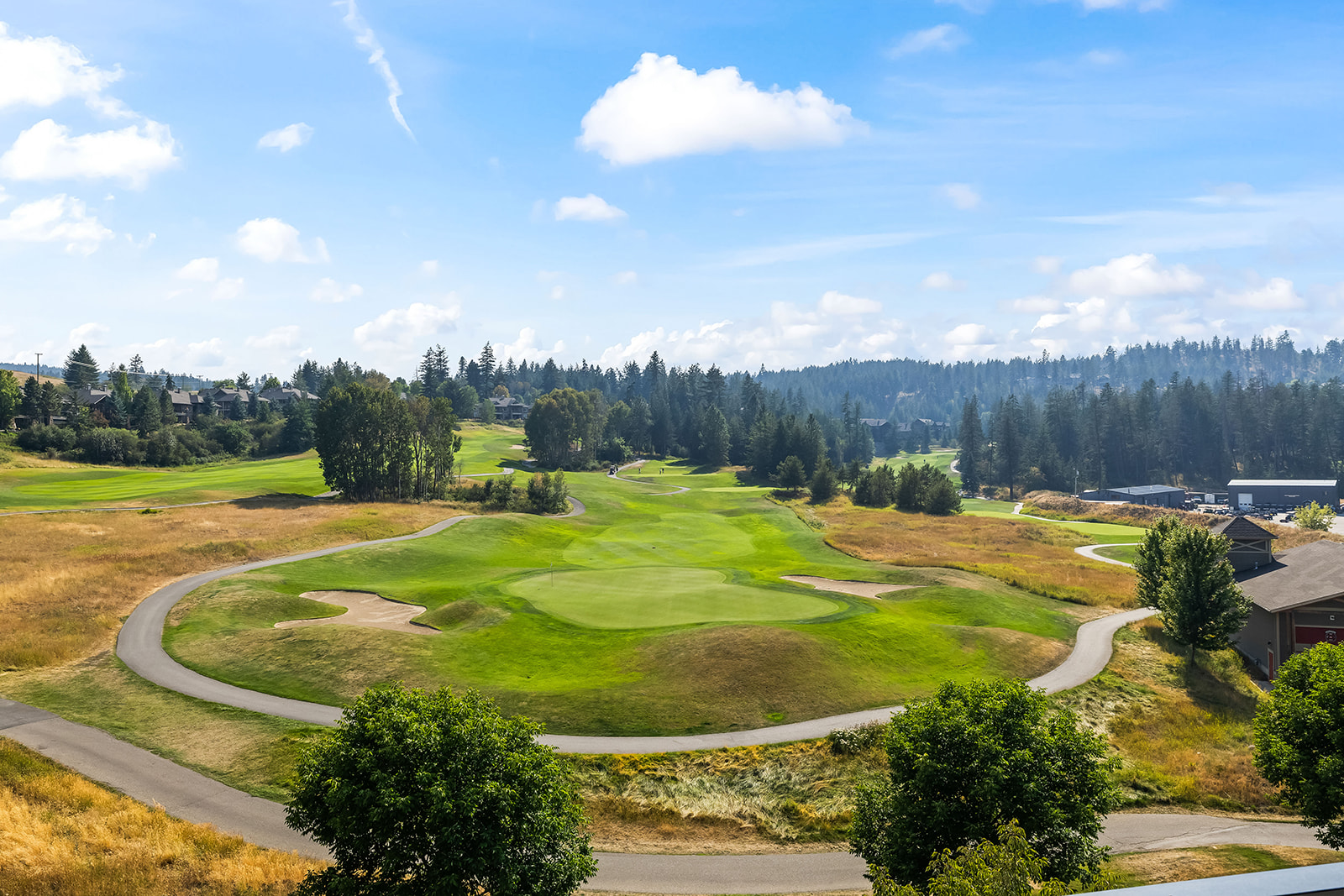 Panoramic golf course with winding paths, sand bunkers, and trees beneath a bright blue sky.