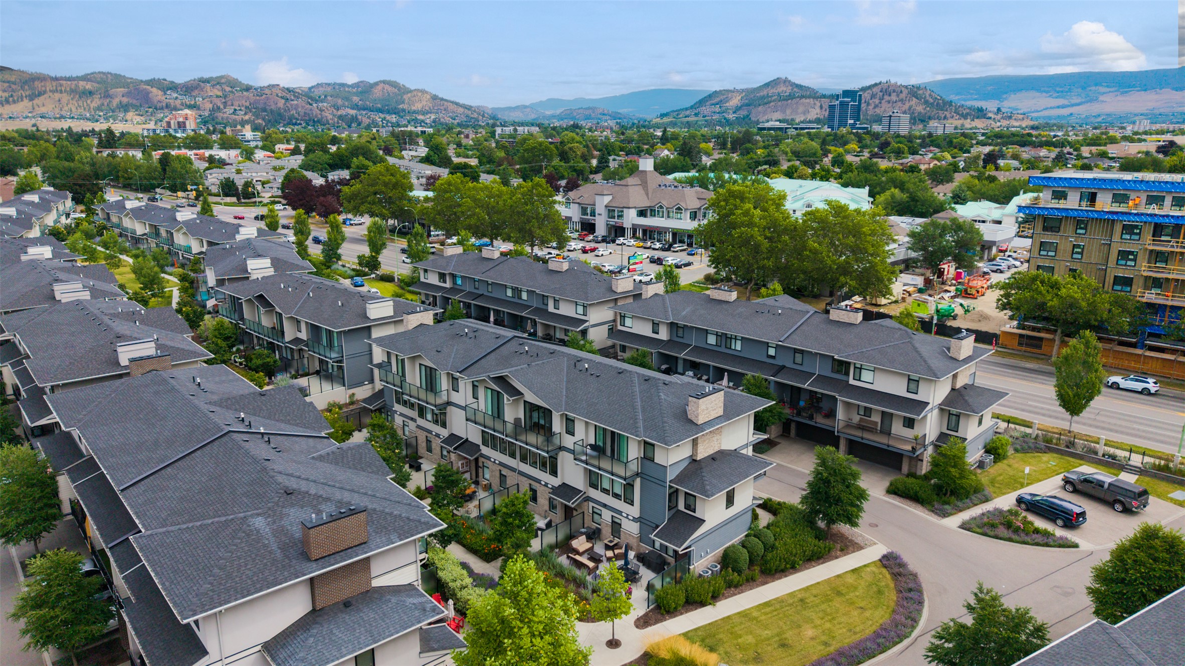 Aerial view of townhouses with landscaped grounds, a curved road, and hills in the distance.