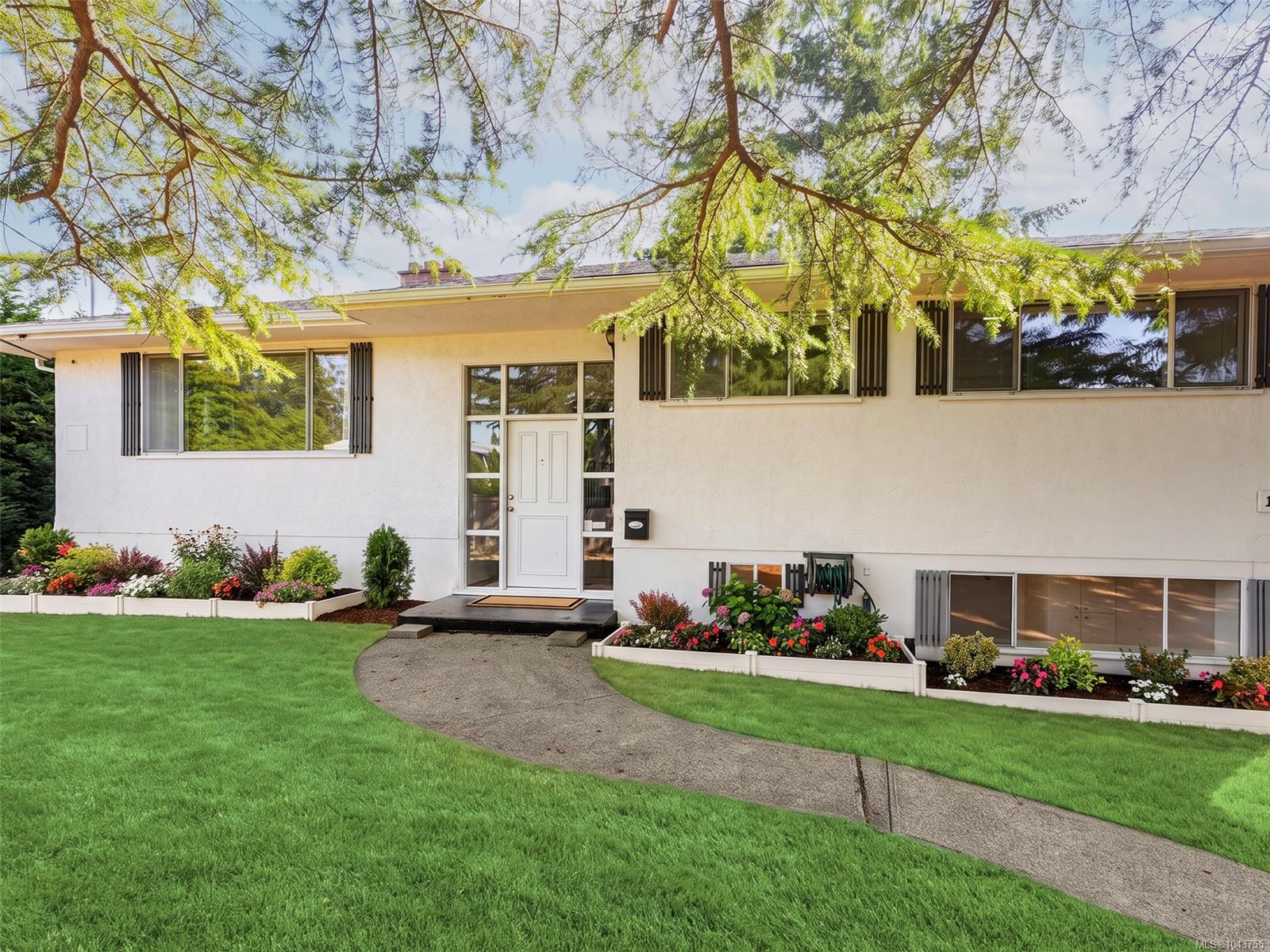 White single-story house with broad windows, flower beds, and a curved walkway across the lawn.