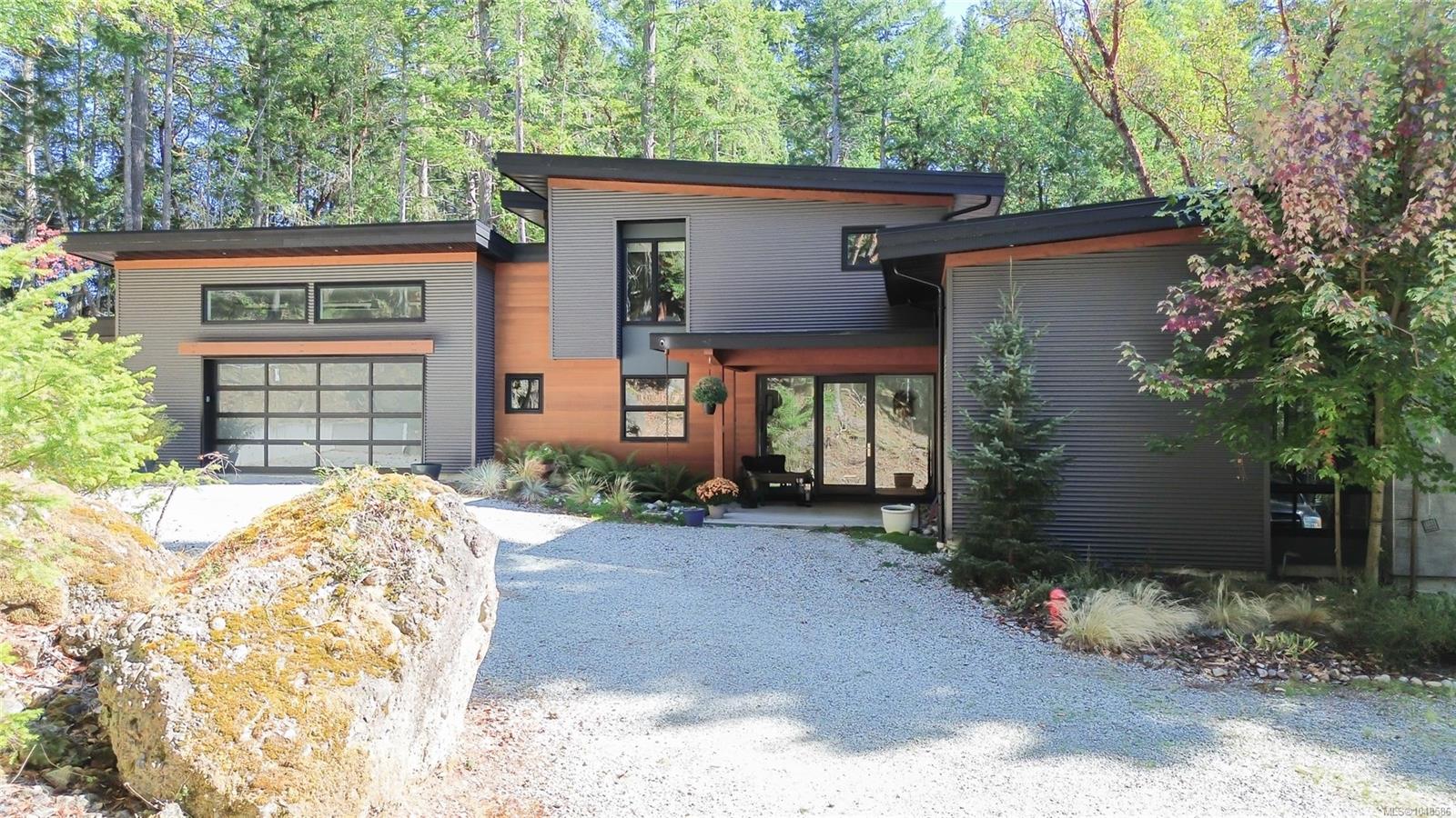 Modern two-story home with gray siding, wood accents, a double garage, and a gravel driveway.