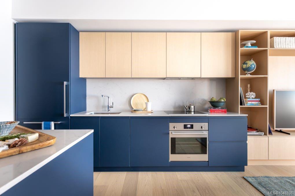 Modern kitchen with navy cabinetry, pale wood cupboards, white stone counters, and open display shelving.