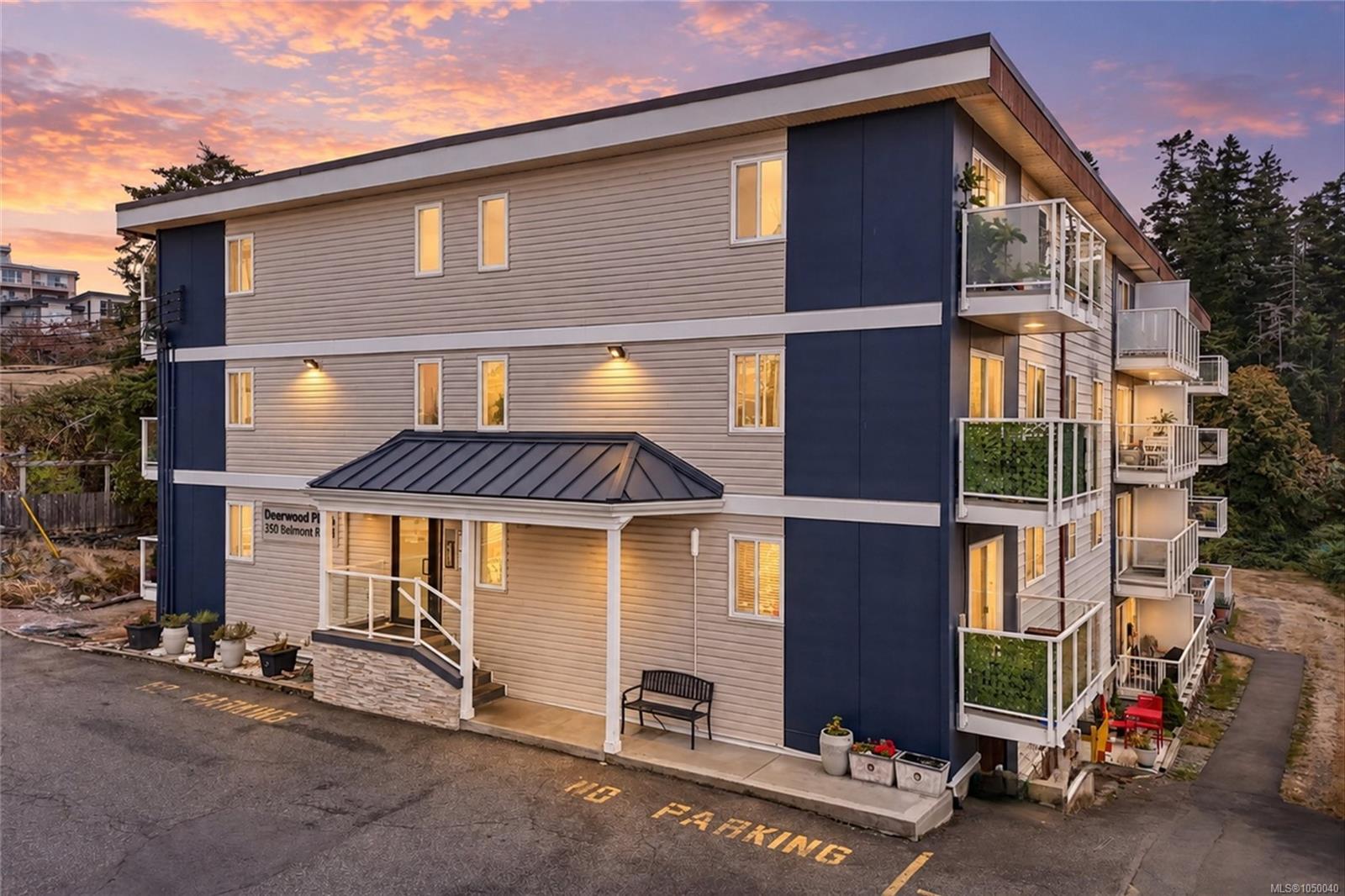 Modern apartment building with multiple balconies and glowing windows beneath a colorful dusk sky.