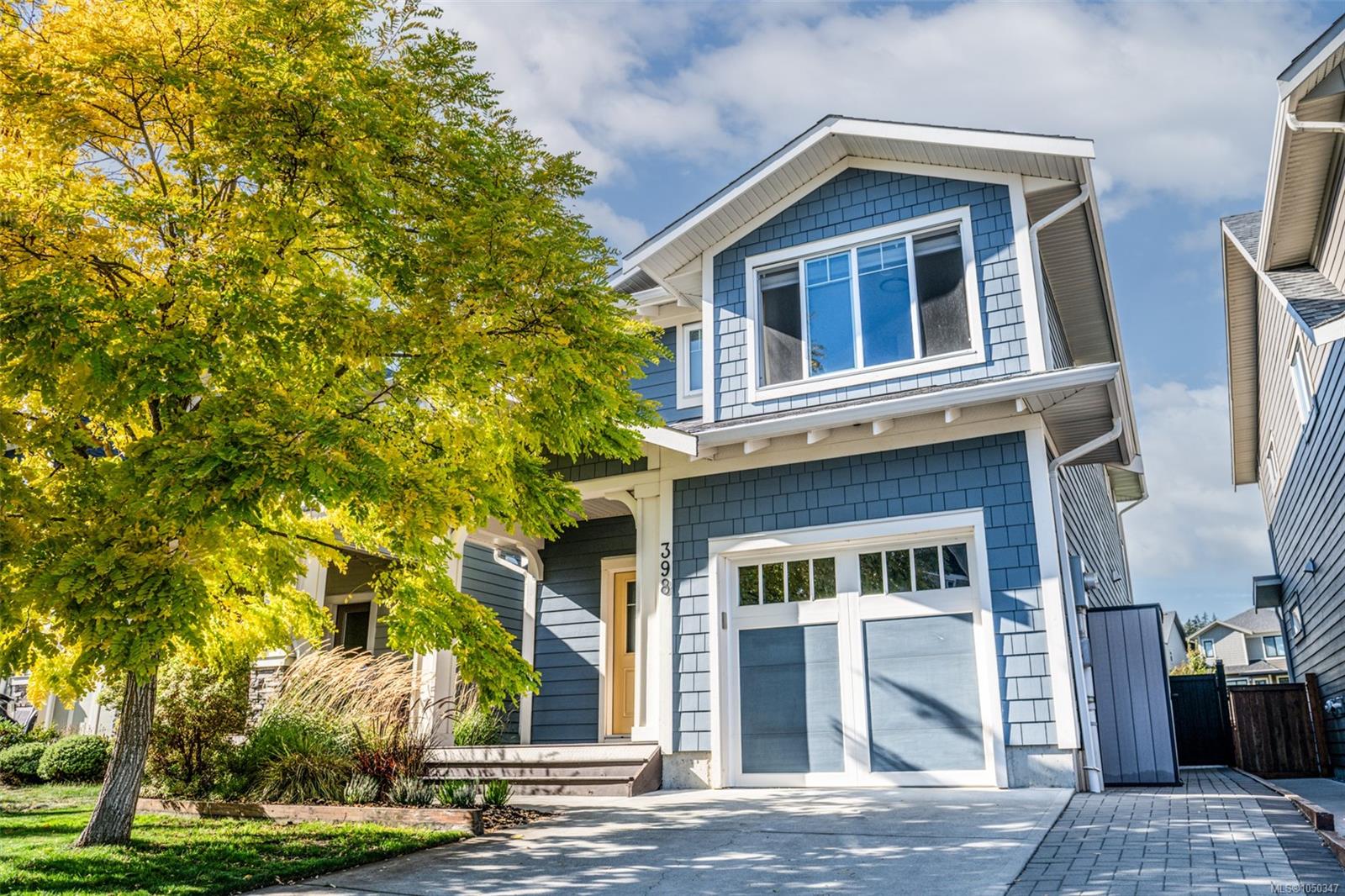 Blue two-story house with white trim and garage, framed by a large yellow-leaved tree.
