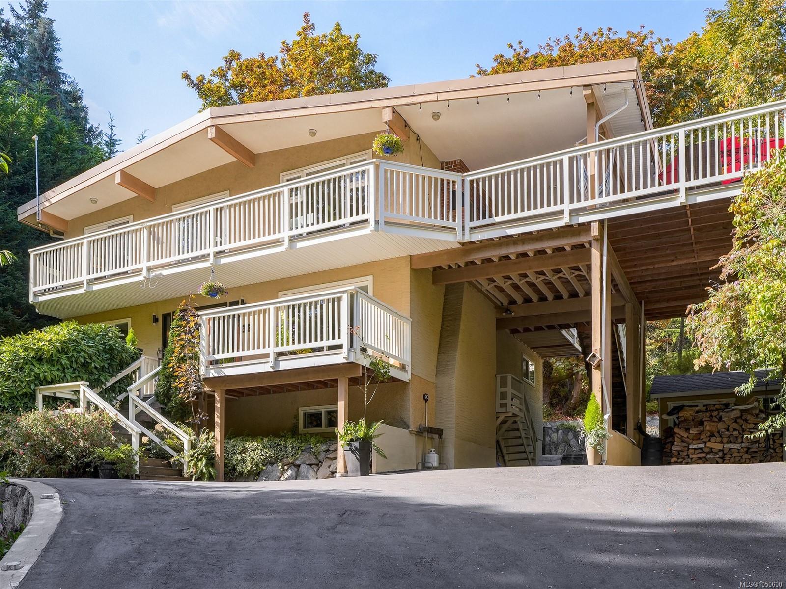 Multi-level tan home with broad white-railed balconies, a covered carport, and mature trees.