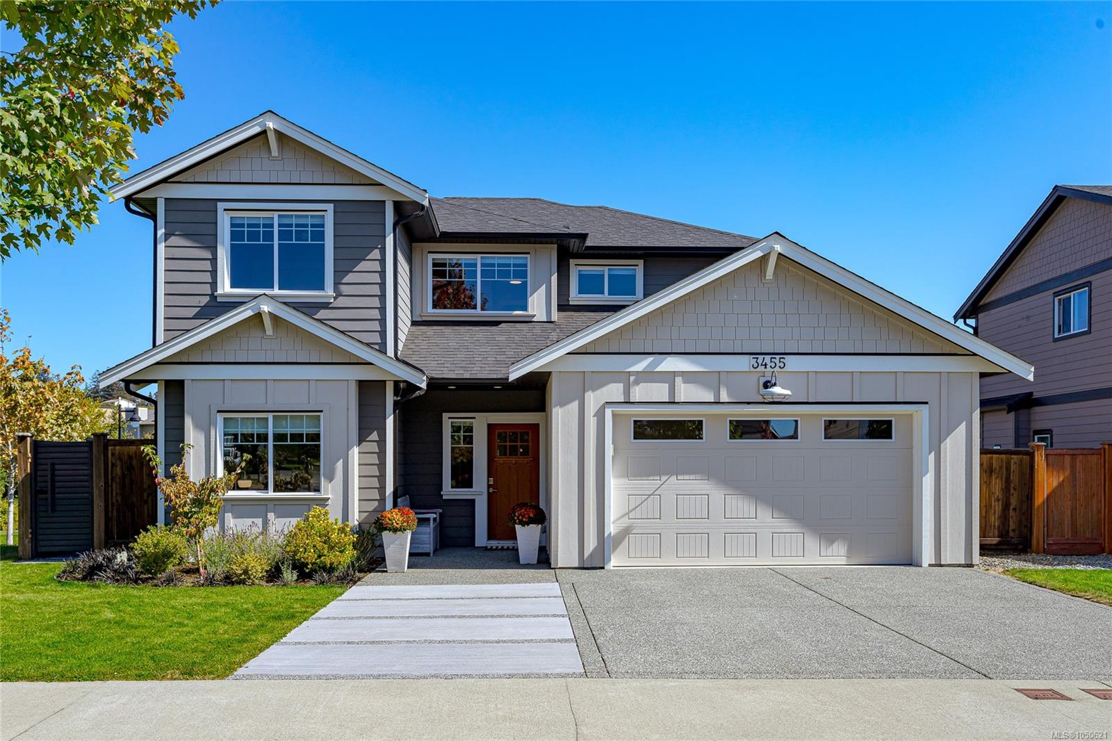 Two-story gray house with white garage, red front door, and landscaped lawn.