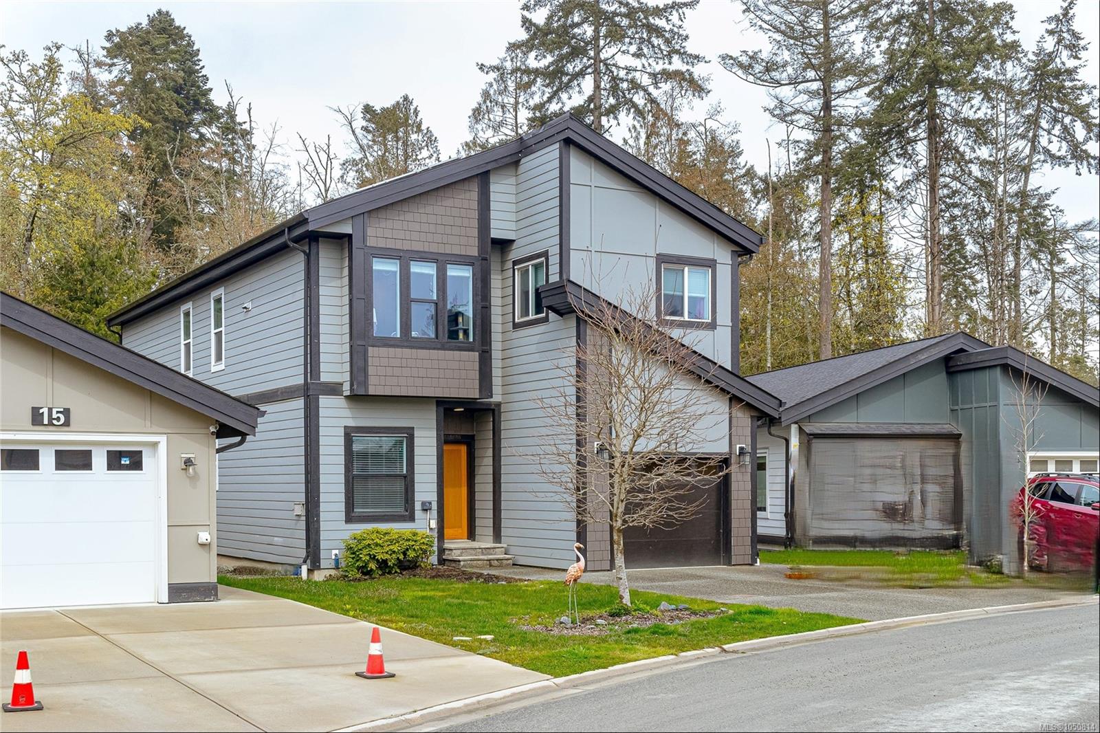 Two-story gray house with dark trim, an orange front door, and an attached garage among tall trees.