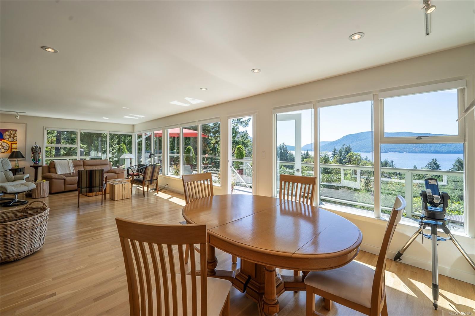 Open-plan living and dining room with expansive windows overlooking water and forested mountains.