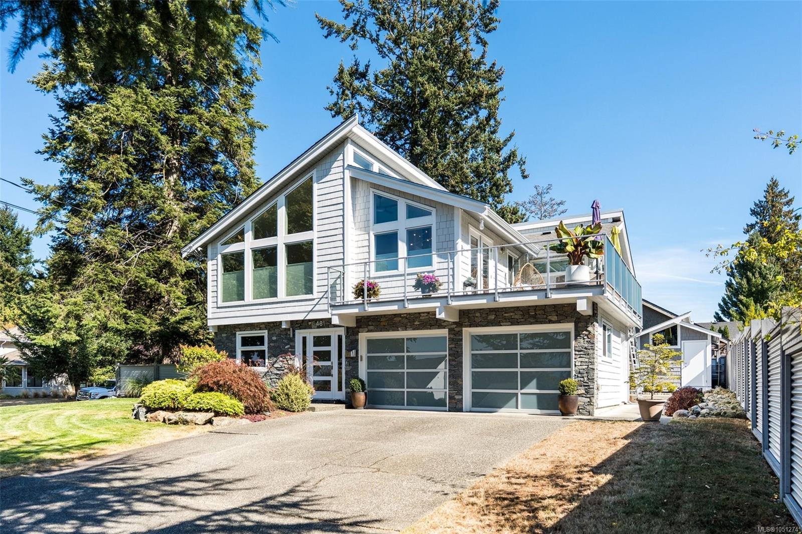 Modern two-story home with a stone lower facade, glass-railed deck, and two garage doors.