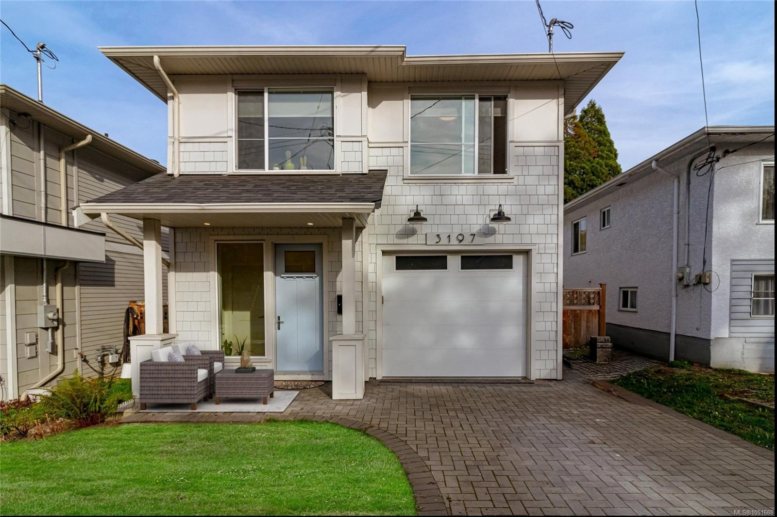 Two-story white house with a covered entry, garage, paved driveway, and patio seating.
