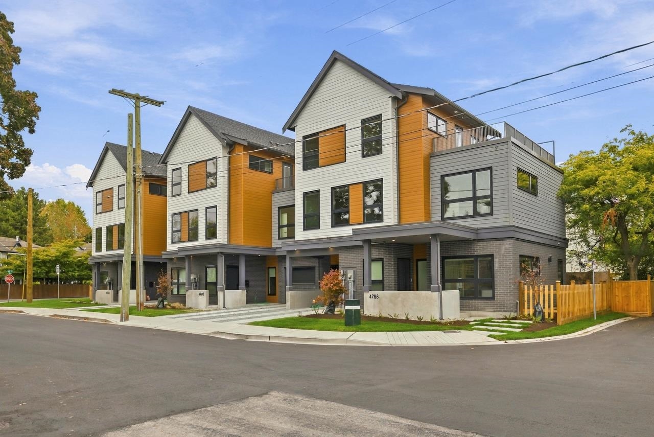 Modern three-story townhouses with orange accents and balconies along a residential street.