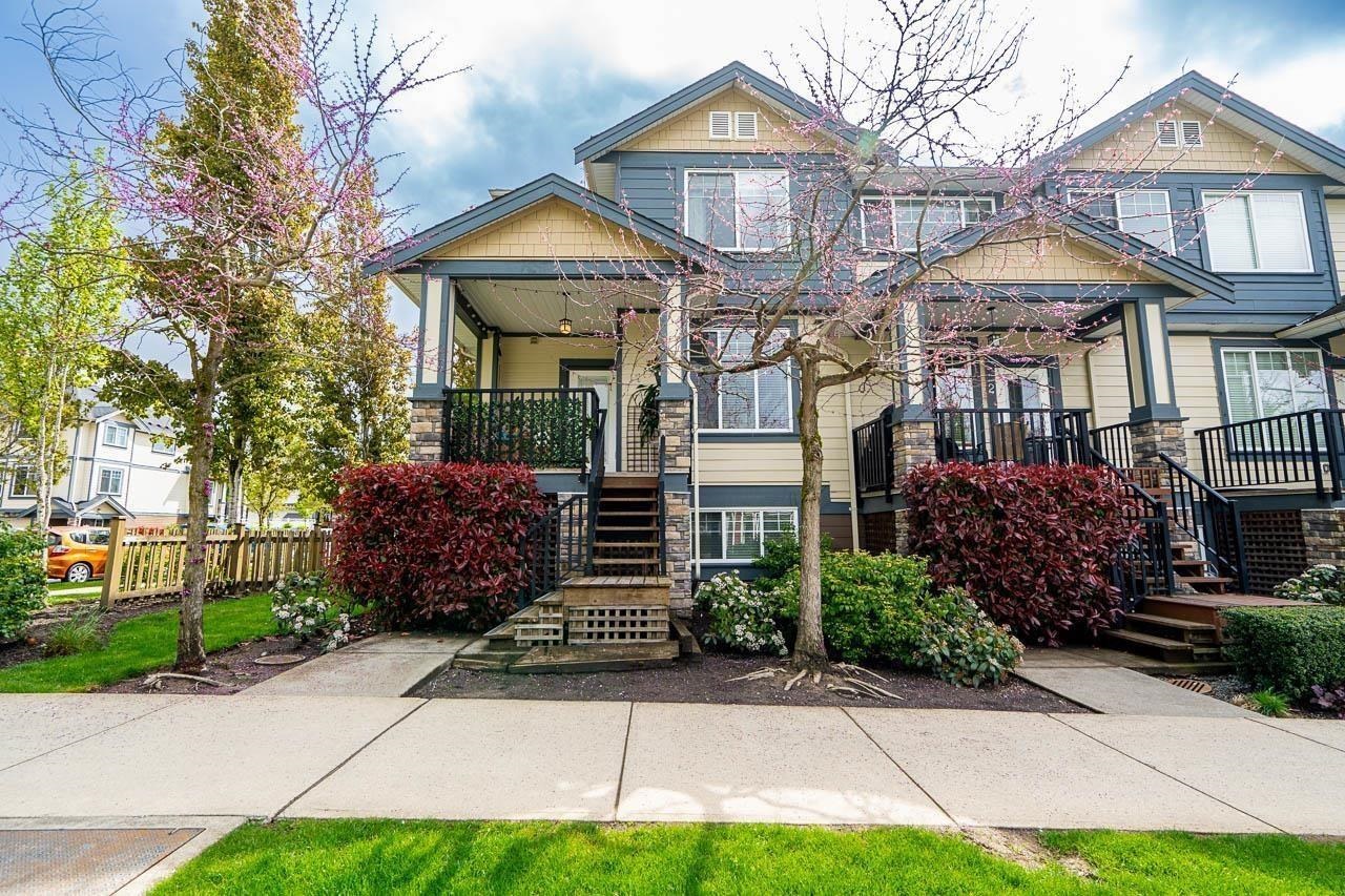 Two-story attached home with blue-gray siding, stone porch columns, and flowering trees.