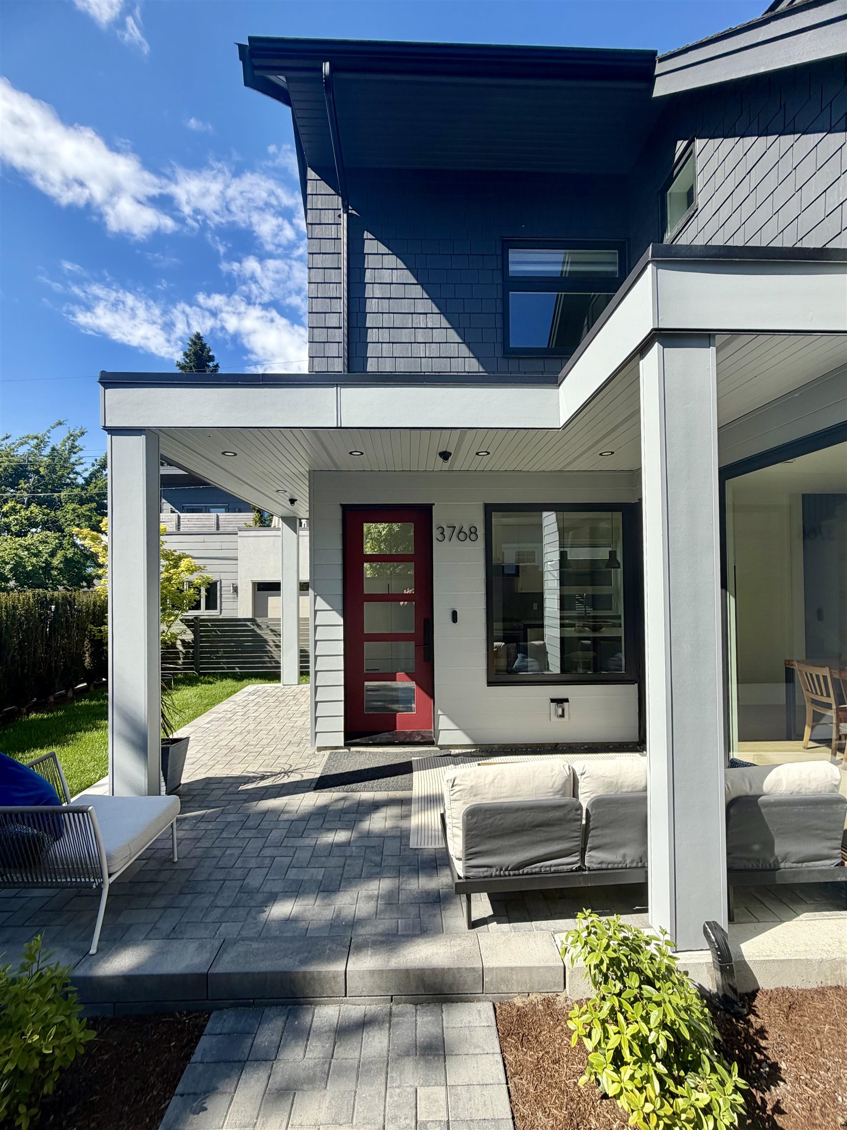 Modern home with gray shingle siding, a red front door, and a covered patio with outdoor seating.