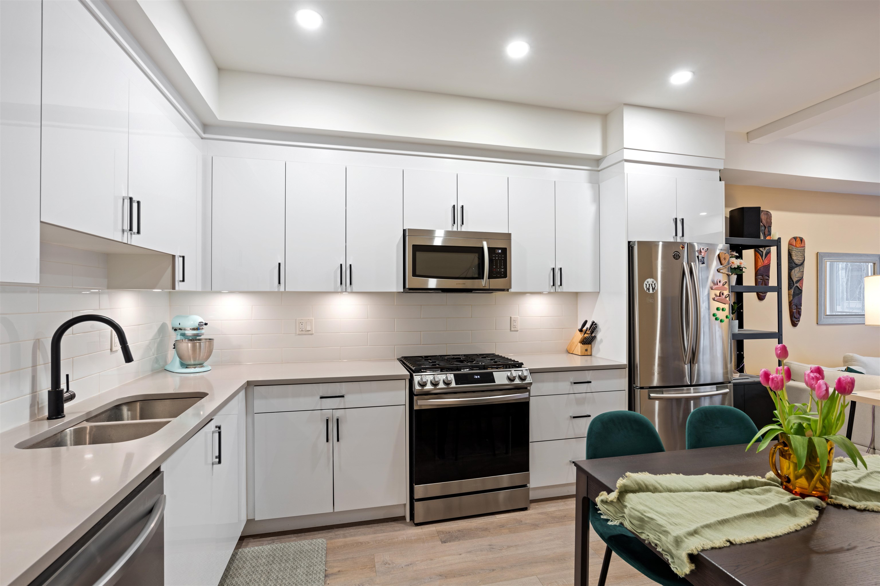 Modern white kitchen with stainless appliances and a dining table set with pink tulips.