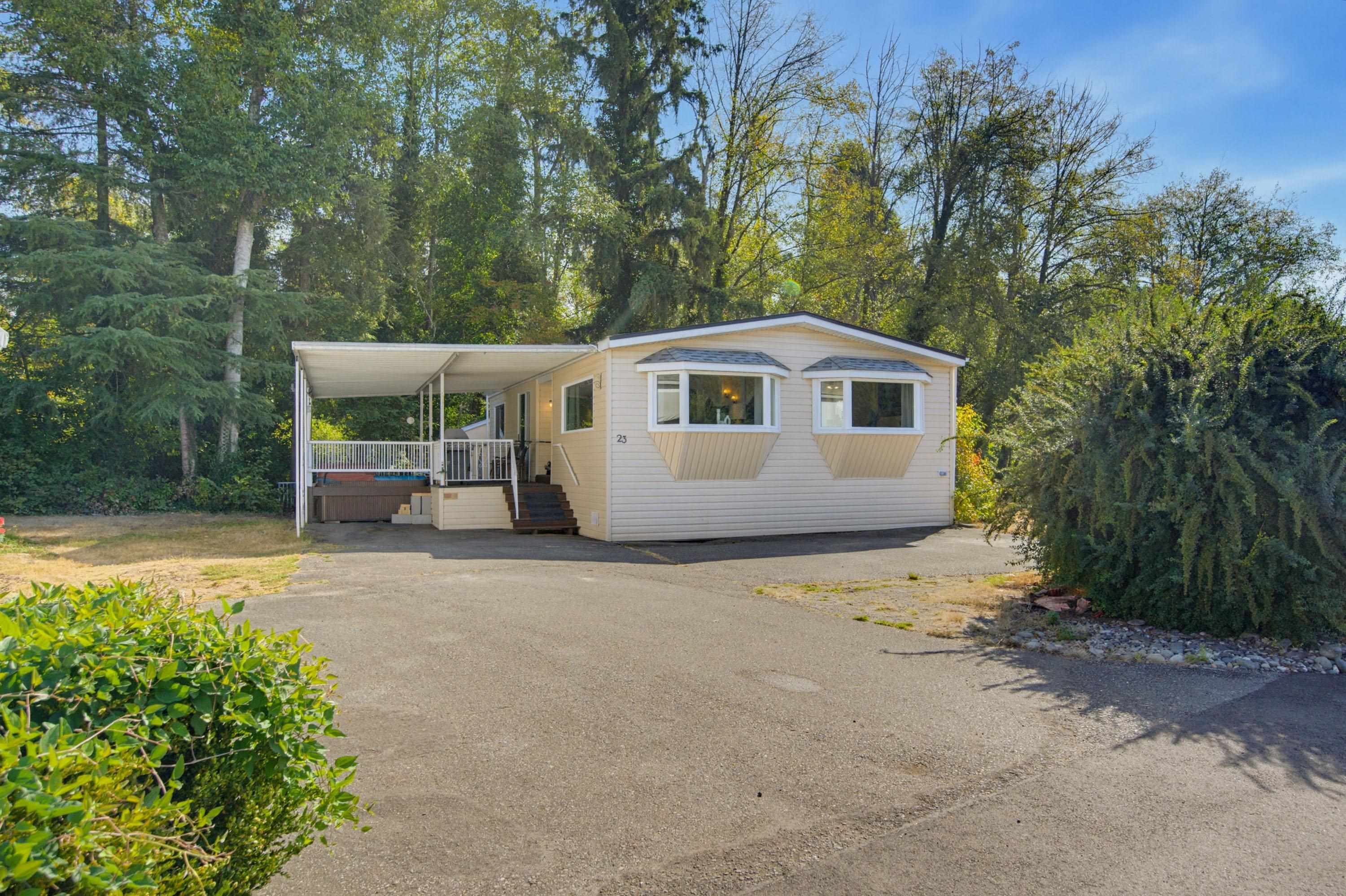 Cream-colored manufactured home with projecting front windows, a covered porch, and a wooded setting.