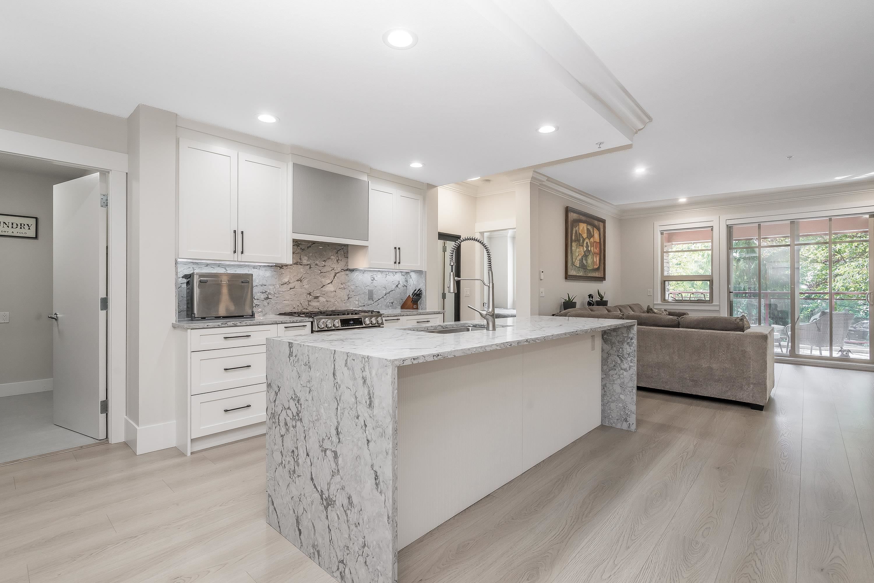 Open-plan kitchen and living room with a large marble-look island and sliding glass doors to a patio.