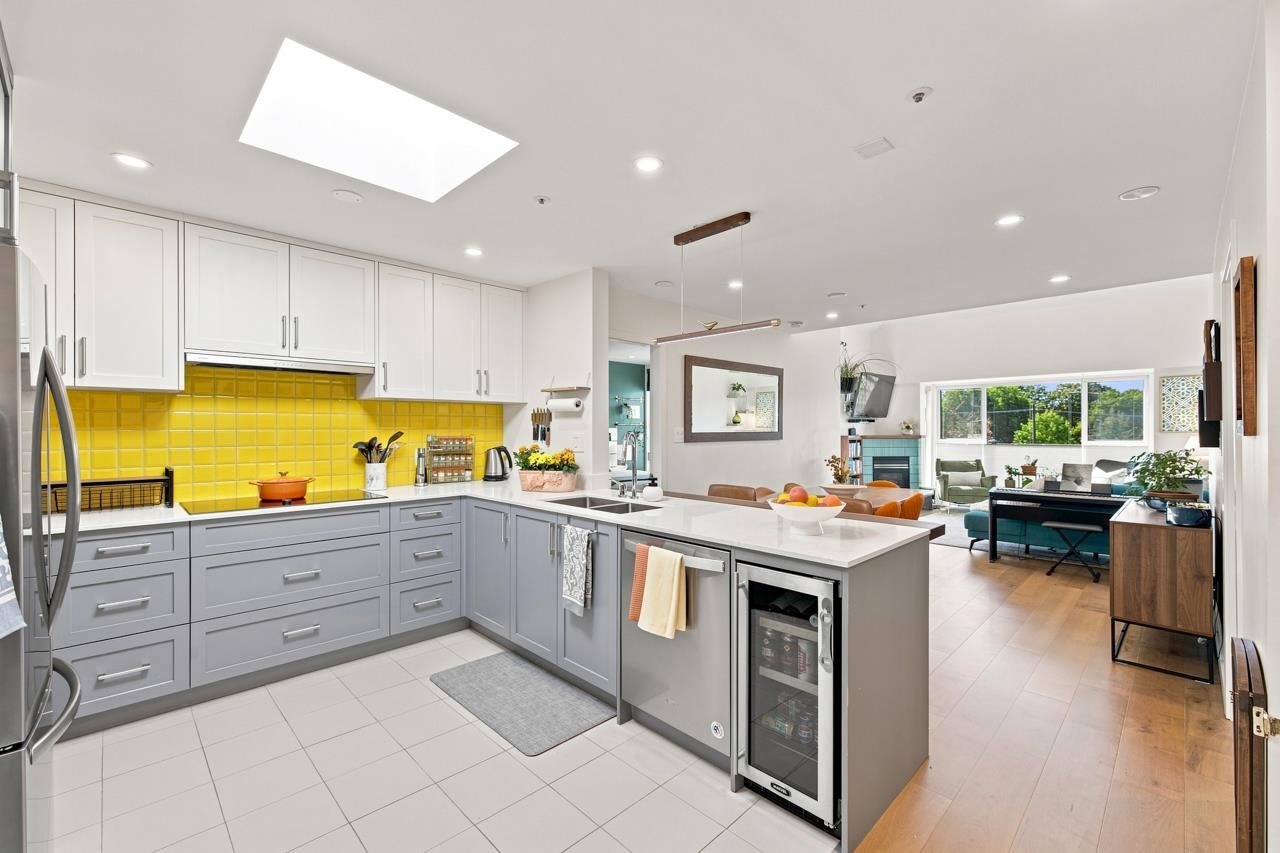 Open-plan kitchen with yellow tile backsplash, gray cabinets, and a large island with beverage refrigerator.