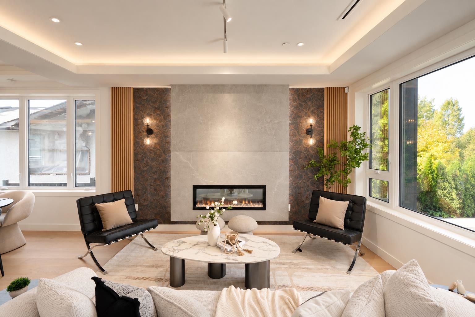 Contemporary living room with a linear fireplace, black lounge chairs, marble coffee table, and large windows.