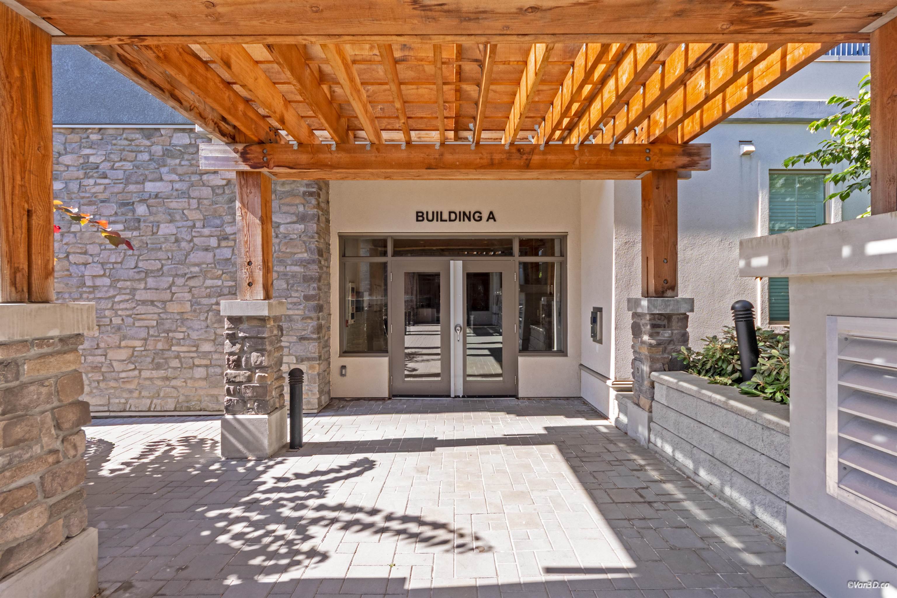 Building A entrance beneath a wooden pergola, with stone walls and glass double doors.
