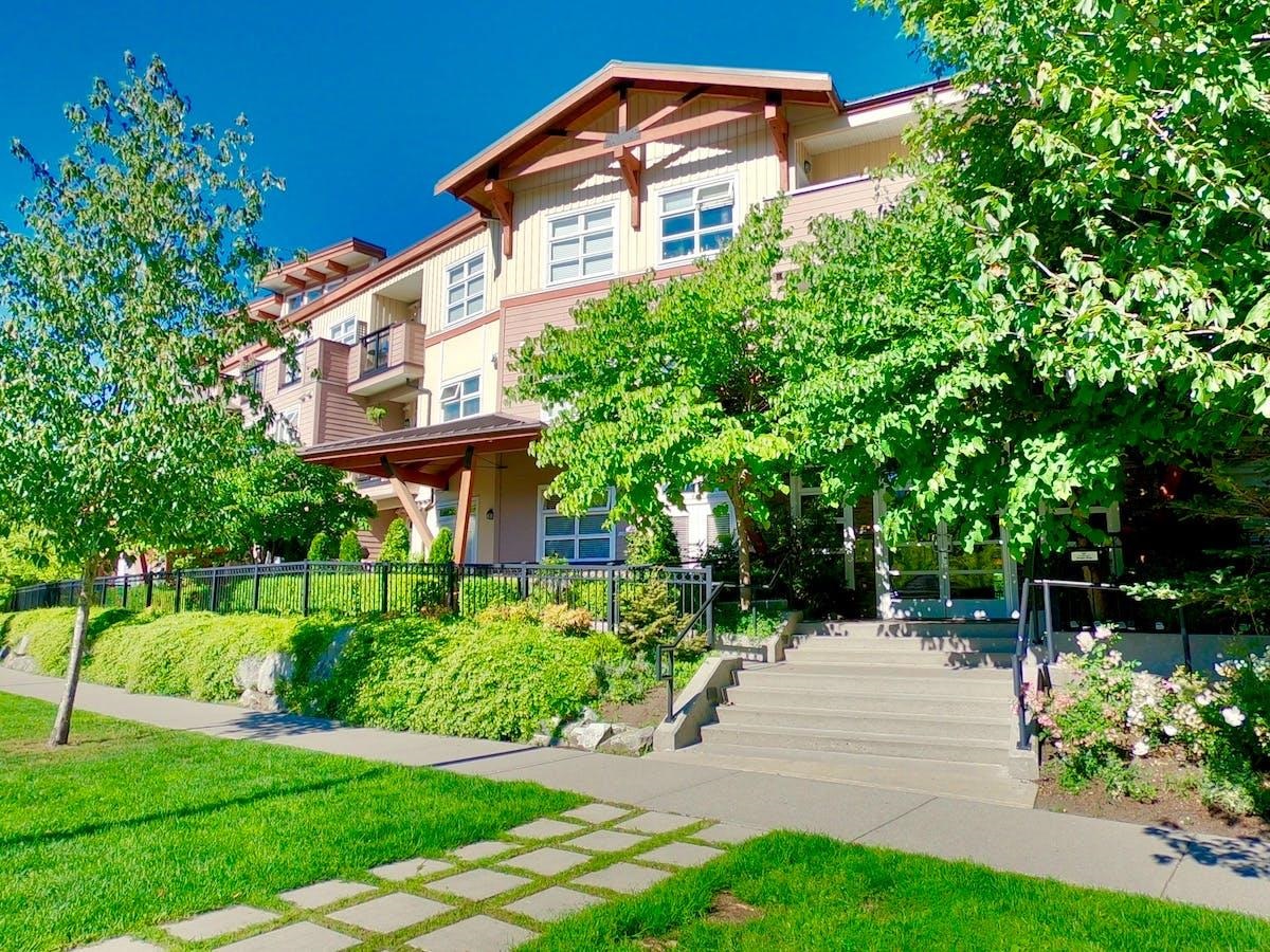 Multi-story residential building with balconies and a leafy, landscaped entrance.
