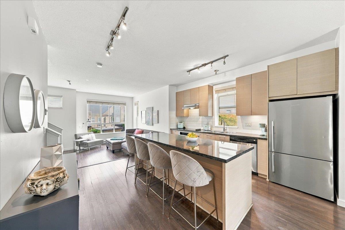 Open-plan kitchen with a large granite island, bar stools, and light wood cabinetry.