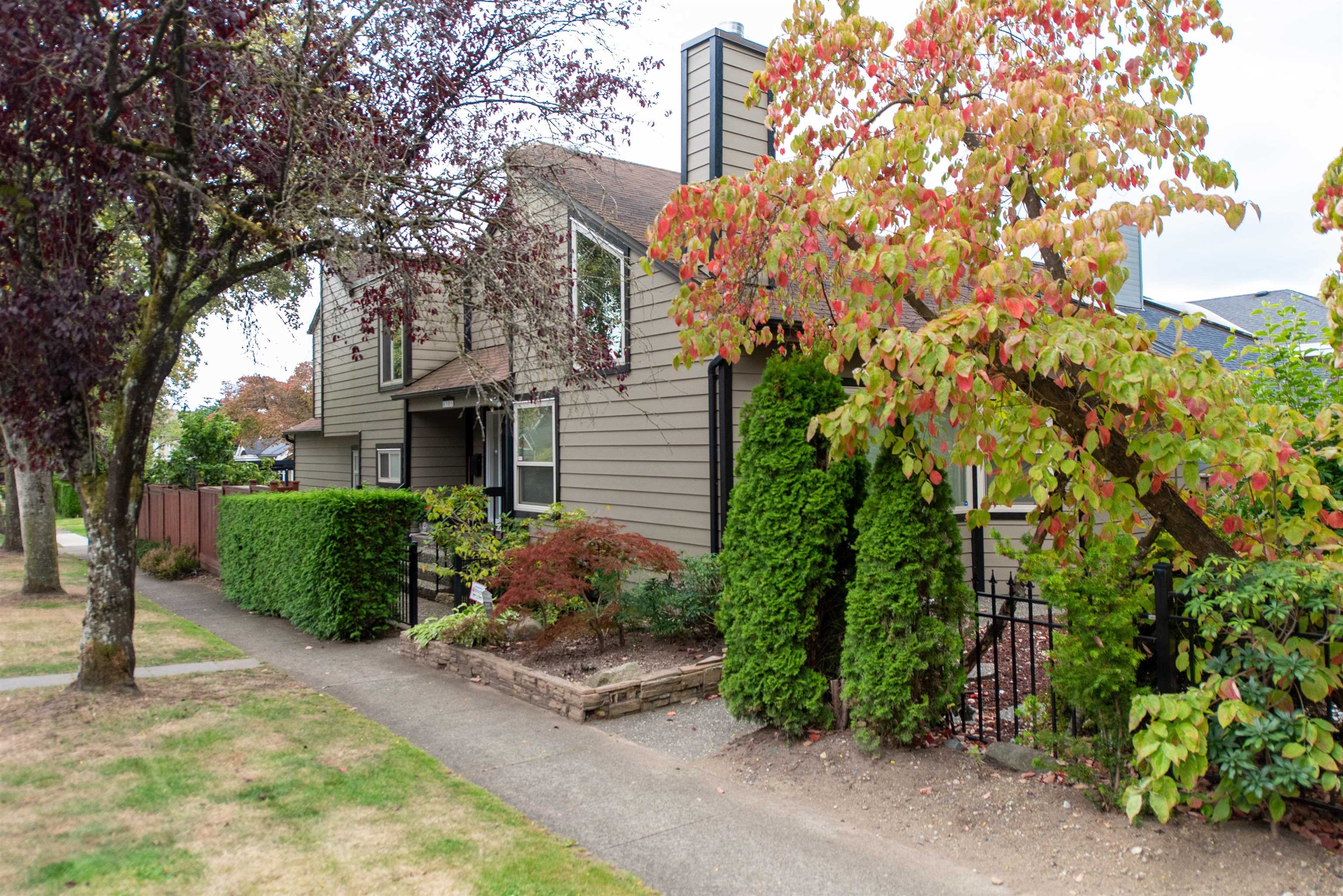 Two-story taupe-sided home framed by landscaped shrubs and colorful autumn trees.