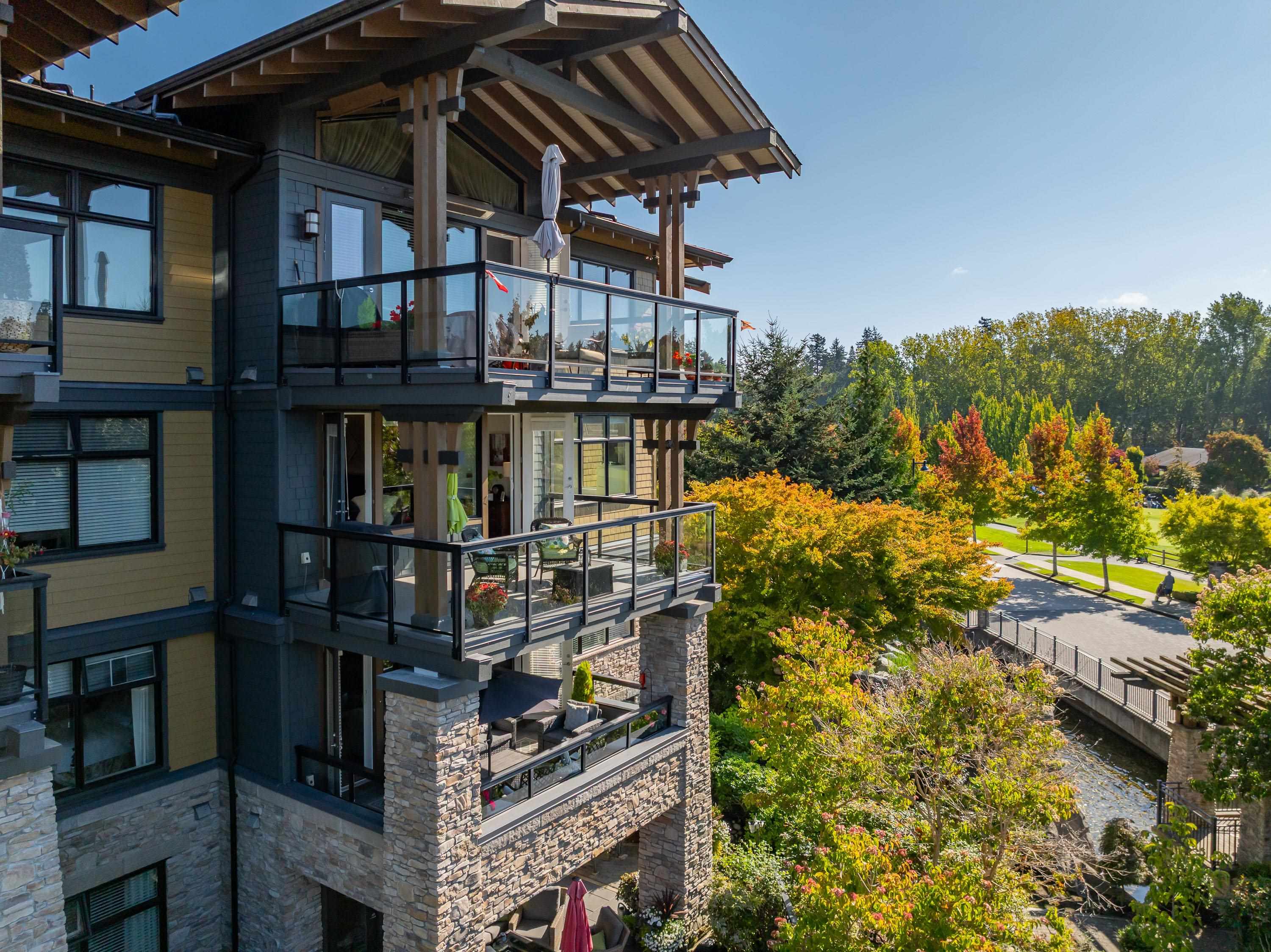 Multi-story home with glass balconies overlooking autumn trees and a creek