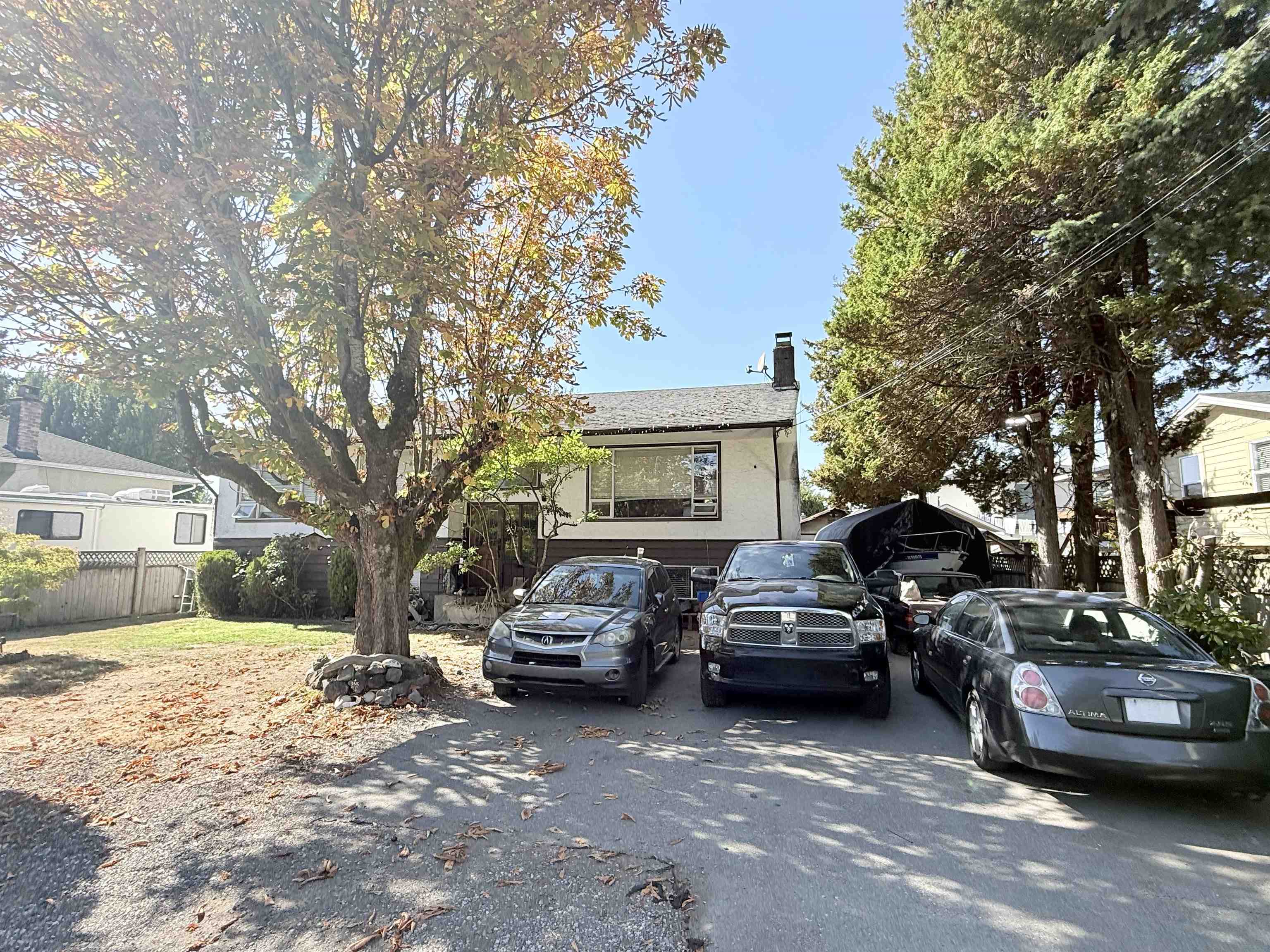 White two-story house behind several parked cars, framed by large trees.