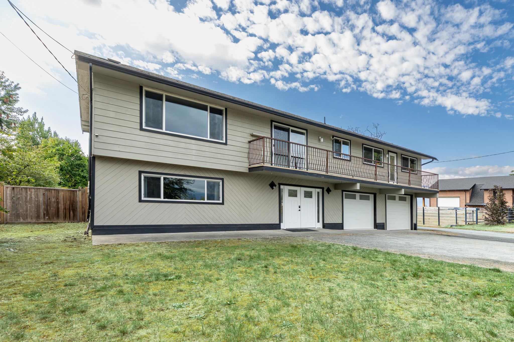 Split-level house with a long balcony, two garage doors, and a patchy front lawn.